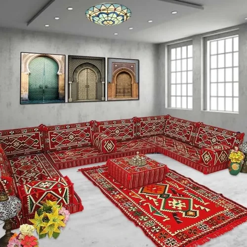 A vibrant red majlis sofa with intricate geometric patterns, paired with matching floor cushions and a rug.